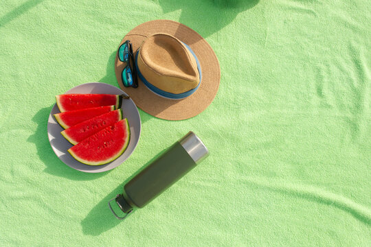 Top view of beach towel with watermelon hat sunglasses and reusable water bottle