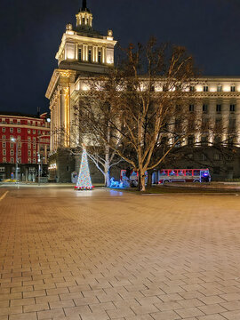 Christmas tree with gifts, toys and festive bus on the city square in the evening. Bulgaria, Sofia