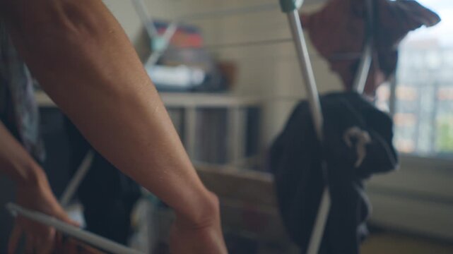 Close-up of hands grabbing clothing from a folding drying rack indoors