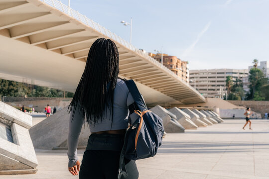 Woman walking under bridge in park with backpack 