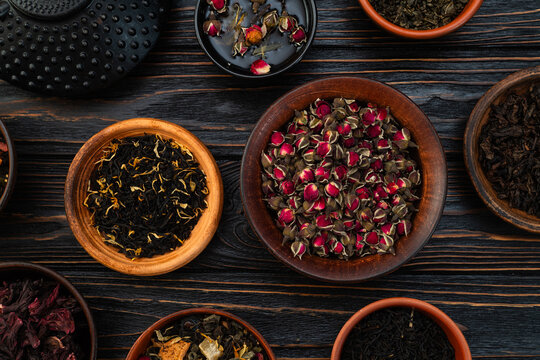 Assorted dry tea leaves and rose buds in ceramic bowls flat lay