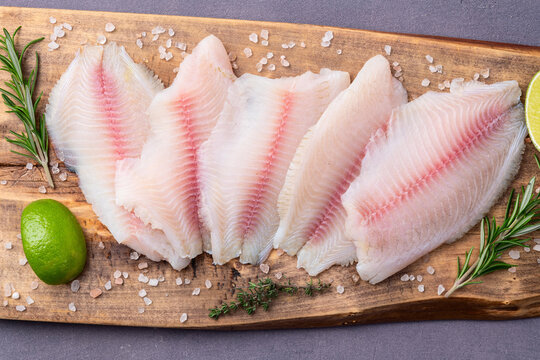 Fresh raw fish fillets on cutting board with lime and rosemary herbs