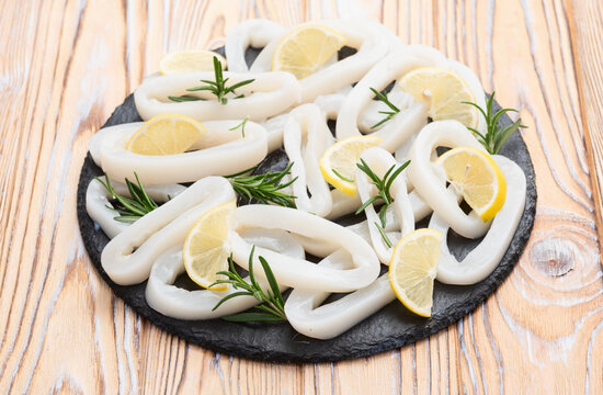 Fresh raw squid rings with lemon and rosemary on wooden board