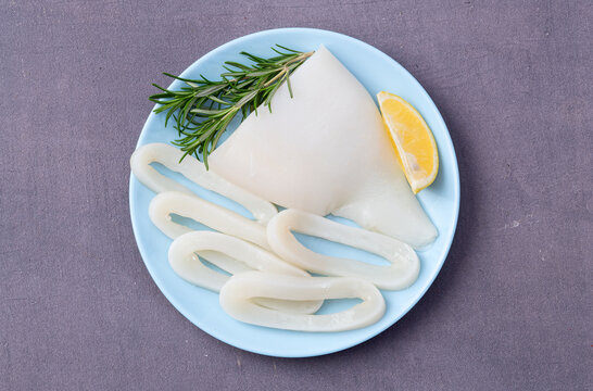 Fresh raw squid rings and fillet with lemon and rosemary on plate