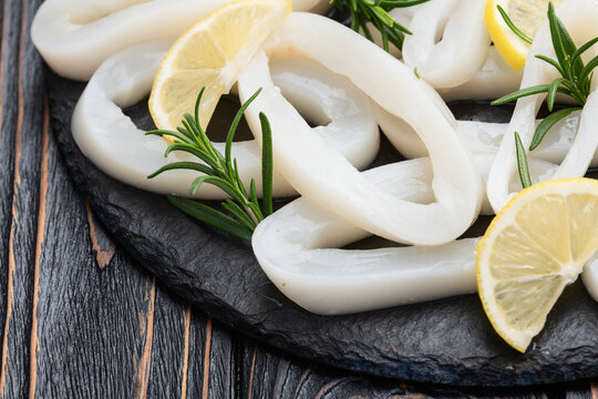 Fresh raw squid rings with lemon and rosemary on dark slate board