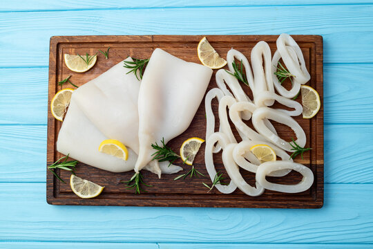Fresh raw squid rings and fillets on wooden cutting board with lemon