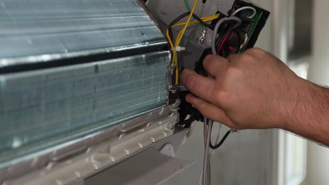 Technician hands adjusting wiring inside wall mounted split air conditioning unit using screwdriver during maintenance service in modern indoor room, with air, conditioning, split, system detail