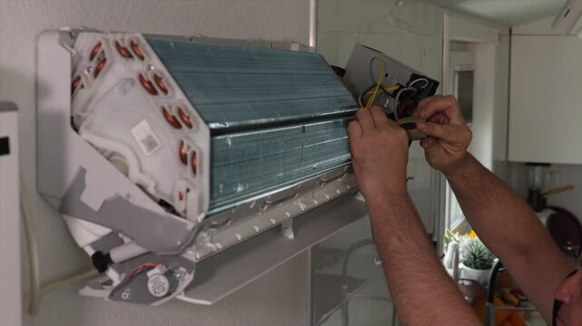 Technician securing wiring inside wall mounted ductless air conditioning indoor unit with front cover removed and evaporator coil exposed during maintenance inspection