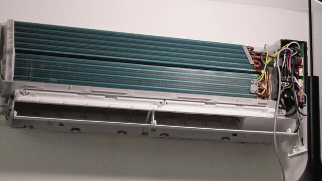 Dismantled wall air conditioner unit with exposed cooling coils and internal electrical circuitry.