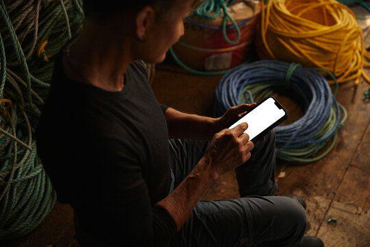 Person using a smartphone while sitting among ropes in a workshop