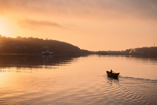 Rowing a small dory boat on calm water during sunset near the shore