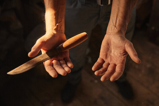 Hardened hands hold a knife ready for a task in a dim light setting