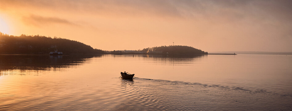 Rowing a small dory boat on calm water during sunset near the shore