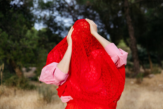 Woman hiding face under red veil in forest