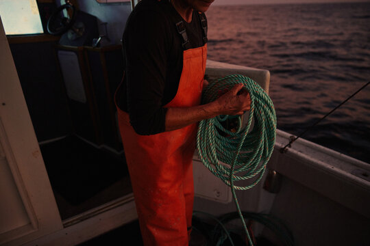 Fisherman prepares gear on boat during evening at sea