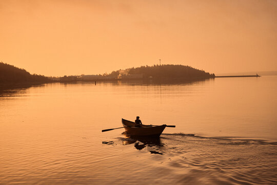Rowing a small dory boat on calm water during sunset near the shore