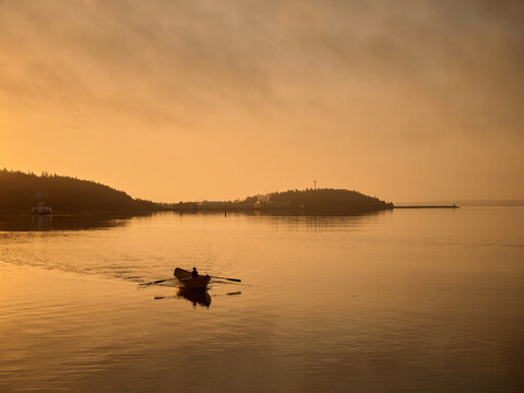 Rowing a small dory boat on calm water during sunset near the shore