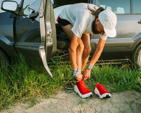 Runner Ties Shoes Near Parked Car on Sunny Day