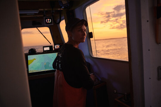 A female boat captain navigates waters at sunset near the coast