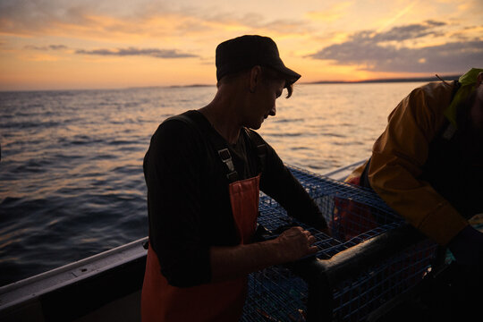 Fishermen preparing traps on a boat at sunset in open water