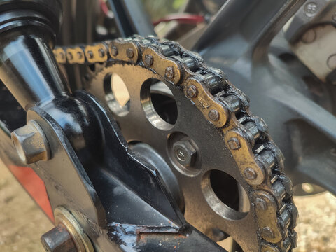 Heavy duty motorcycle rear drive sprocket and oiled roller chain close-up, essential power transmission parts for bike maintenance, replacement, and tuning.