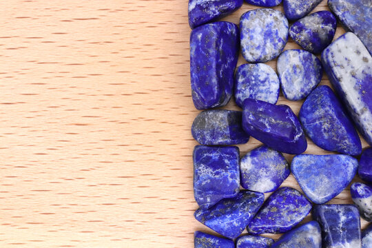 Collection of rough cut blue lapis lazuli gemstones displayed on light wooden surface for mineral photography