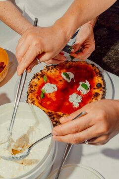 Chefs adding fresh cheese and basil to a hot pizza