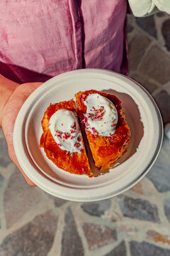Hands holding a plate with a crispy pastry dessert topped with cream