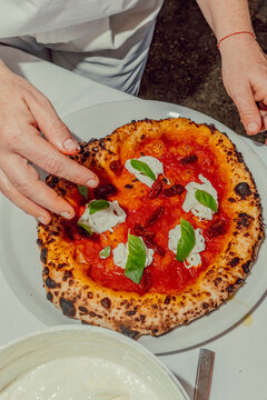 Chef garnishing a fresh Neapolitan pizza with basil leaves