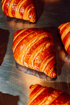 Freshly baked golden croissants on a stainless steel baking sheet