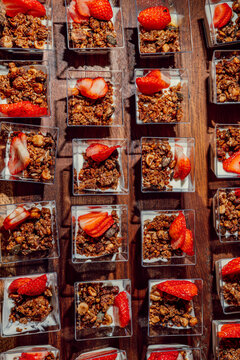 Rows of individual yogurt parfaits with granola and strawberries 
