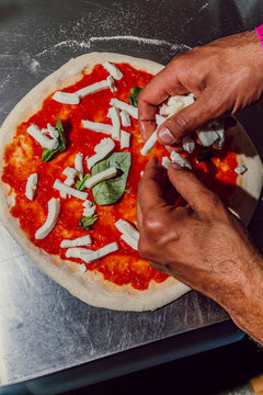 Chef using hands to spread mozzarella cheese on fresh pizza dough