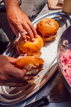 Chef's hands assembling artisan burgers on a silver tray