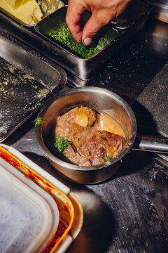 Chef garnishing cooked meat in a pot with chopped chives