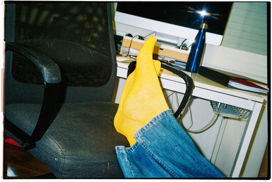 a man rests his legs on an office chair in yellow socks, 35mm film