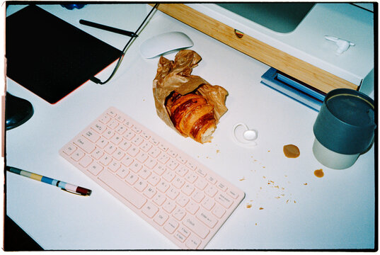 a croissant rests beside a keyboard on an office desk, 35mm film