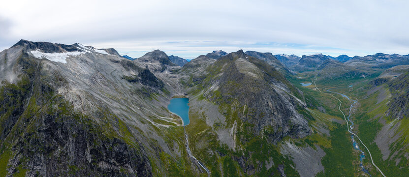 Aerial view of a glacial lake nestled between rugged mountain peaks with rocky slopes and green vegetation in the valley of Valldal, More og Romsdal, Norway.