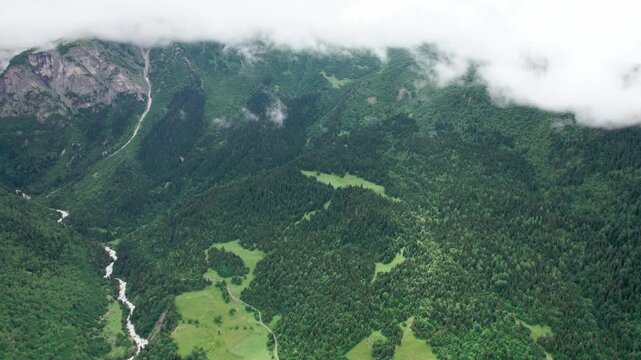 Aerial drone flight over a lush green mountain valley with a crystal-clear river flowing through the gorge. Towering peaks, pristine summer wilderness and breathtaking alpine scenery in the Caucasus