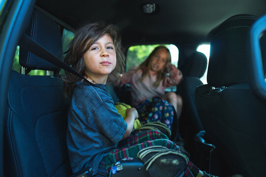 Two boys sitting in the back seat of a car with bags and blankets