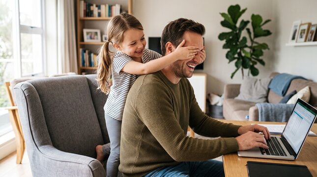 Playful Daughter Covering Her Father&rsquo;s Eyes While He Works on a Laptop at Home During a Joyful Family Break and Bonding Moment