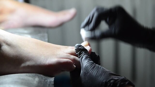Professional pedicure master smoothing and buffing toenails with a nail buffer during a salon treatment. Close-up of foot care procedure preparing nails for the next stage of pedicure.