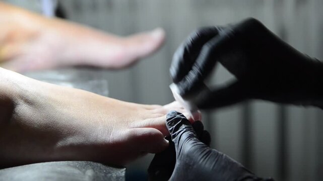 Professional pedicure master smoothing and buffing toenails with a nail buffer during a salon treatment. Close-up of foot care procedure preparing nails for the next stage of pedicure.