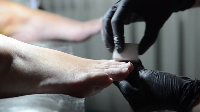 Professional pedicure master smoothing and buffing toenails with a nail buffer during a salon treatment. Close-up of foot care procedure preparing nails for the next stage of pedicure.