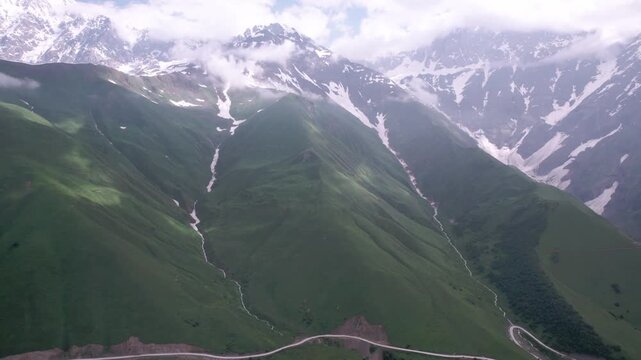 Epic cinematic drone flight above majestic green mountain valley with glaciers, winding serpentine road and lush Caucasus peaks in Svaneti, Georgia. for travel, meditation, wellness and nature project