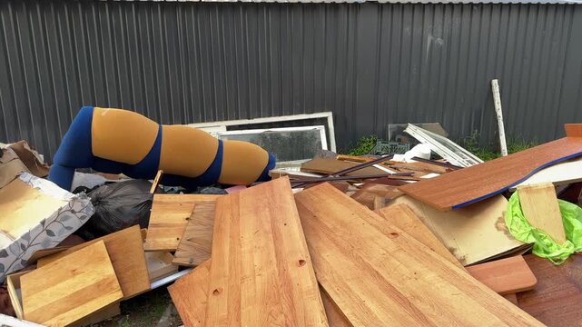 Old sofa, wooden boards and trash bags dumped in a pile near a metal fence. Bulky waste, illegal dumping, household garbage