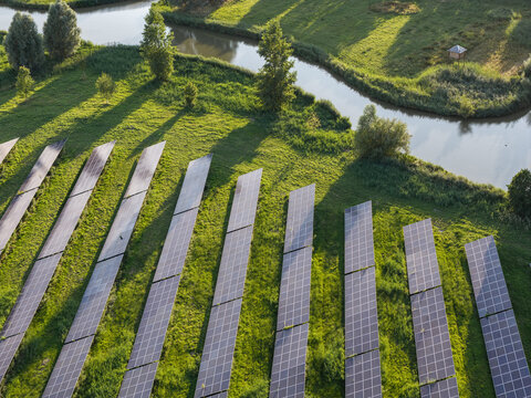 Aerial view of the Zonnepark solar farm featuring rows of photovoltaic panels set in a lush green field beside a winding canal in Purmerend, North Holland, Netherlands.