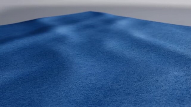 Cobalt blue fabric surface with subtle shifting folds and shallow central peak, viewed from low angle with soft studio light, showing gentle settling texture across wide plane