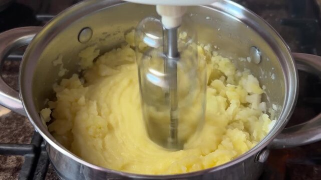 Electric whisk whipping soft mashed potatoes in a stainless steel pot. Home cooking, dinner preparation, creamy potato dish