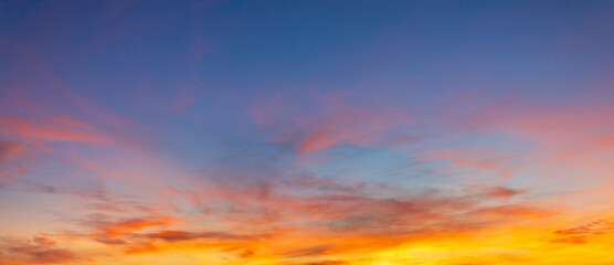 Fototapeta premium Vibrant colorful sunset sky with dramatic clouds and glowing gradient twilight horizon,A breathtaking panoramic view of a vibrant colorful sunset sky filled with dramatic wispy clouds, transitioning.