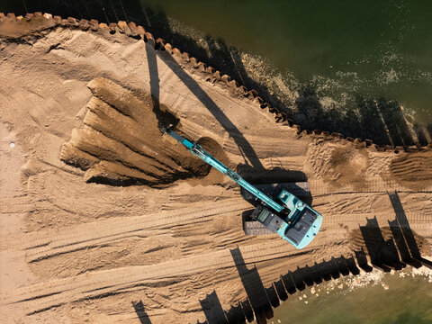 Aerial view of an excavator working on the sandy shore of Lampedziu papludimys, with metal sheet piling along the water edge in Kaunas, Kauno apskritis, Lithuania.